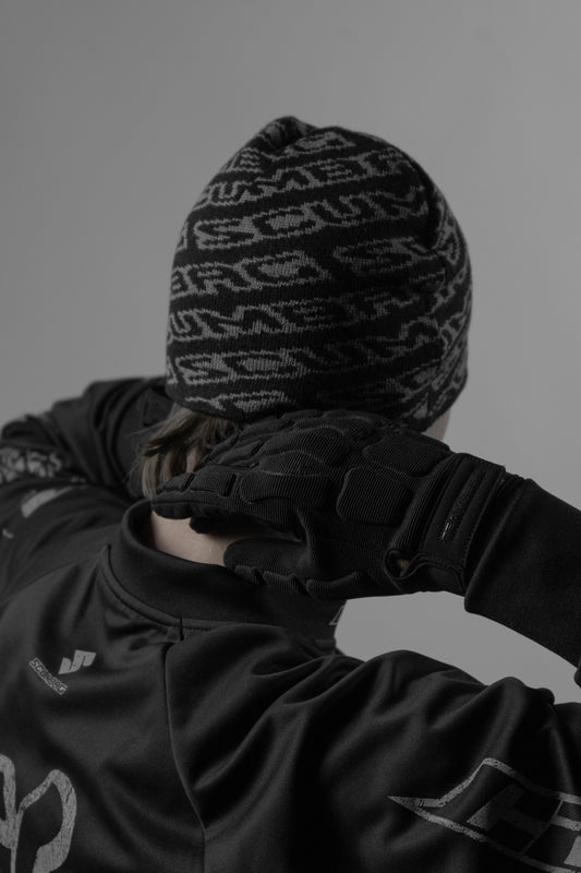 Person wearing a patterned beanie and dark jacket against a gray background